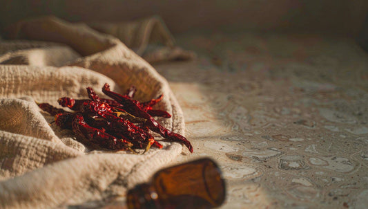 Dried red cayenne chilies on linen beside an amber glass bottle in warm window light